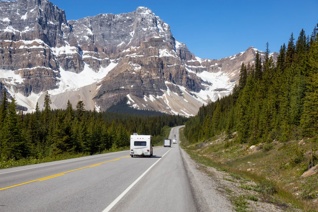 VR roulant sur une route entourée de forêts et de montagnes enneigées dans l’Ouest canadien, illustrant un itinéraire pittoresque entre Montréal et Vancouver.
