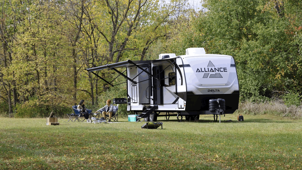 Roulotte Alliance Delta stationnée sur un terrain verdoyant avec deux campeurs assis sous l’auvent, illustrant la solidité et la protection contre les infiltrations des meilleures roulottes de camping.