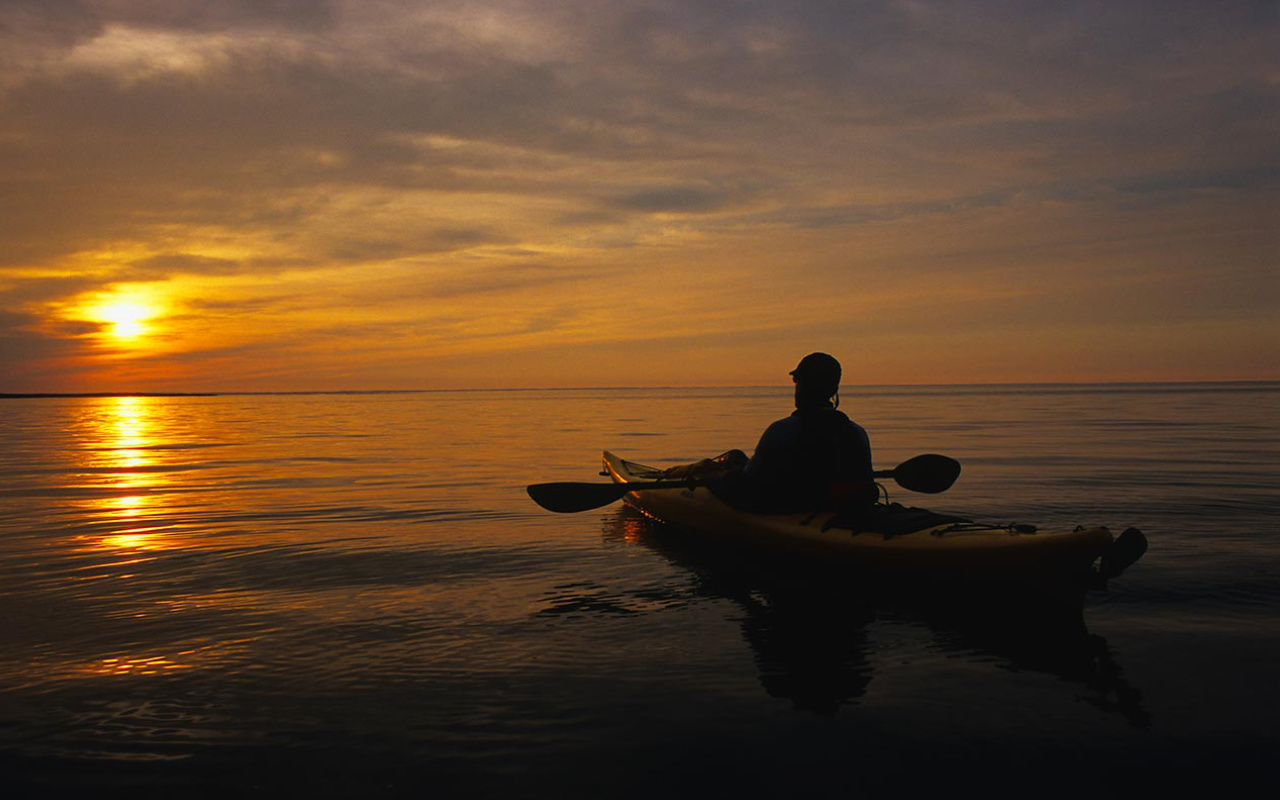 homme dans un kayak sur un grand lac au coucher de soleil