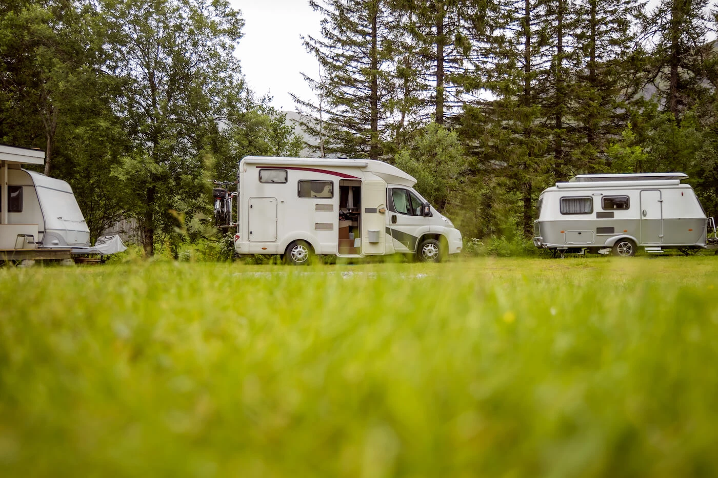 Deux petites roulottes et un motorisé au centre garés au bord des arbres.