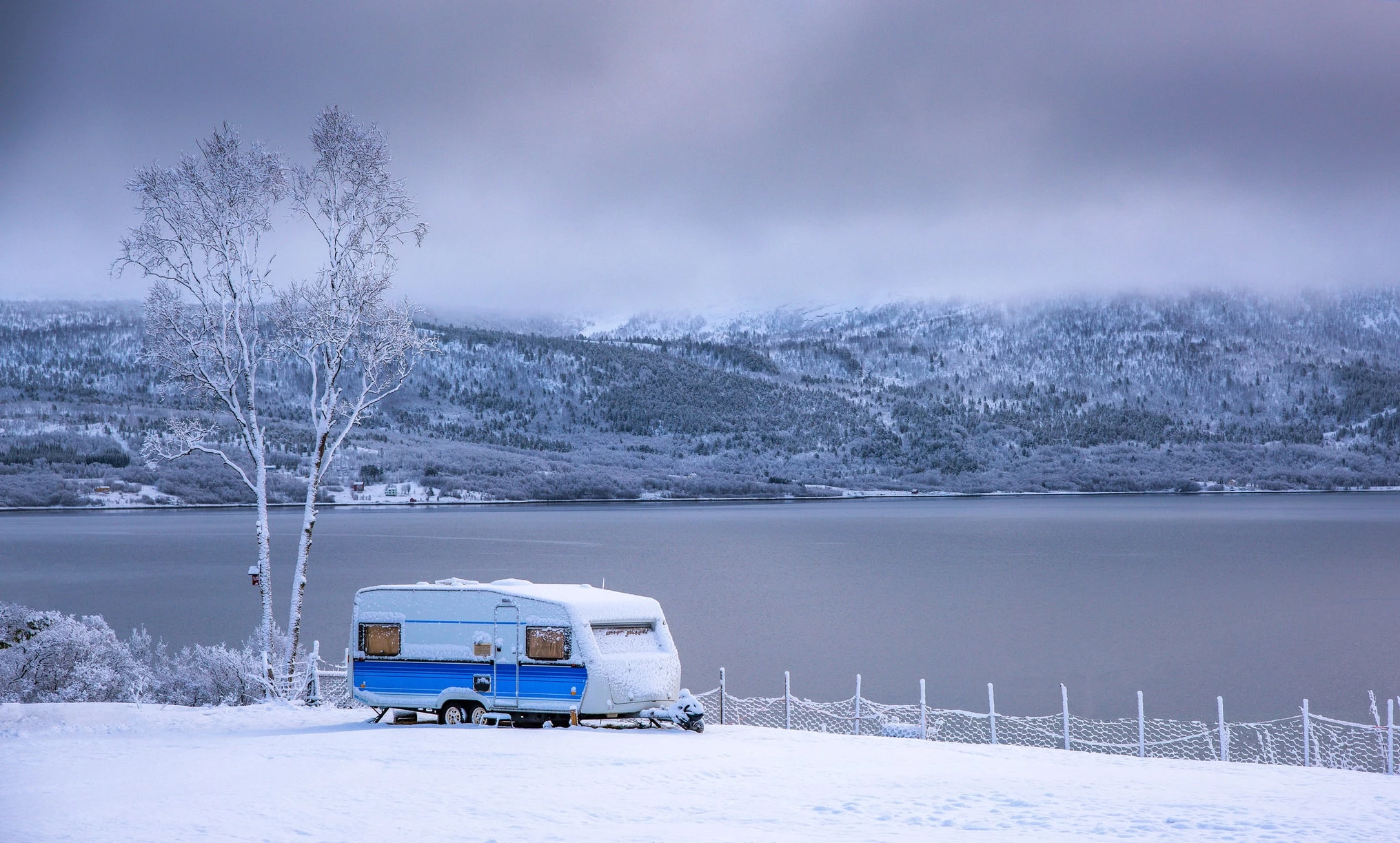 Une roulotte installée sur une terre face à un fleuve et aux montagnes pendant la saison d'hiver