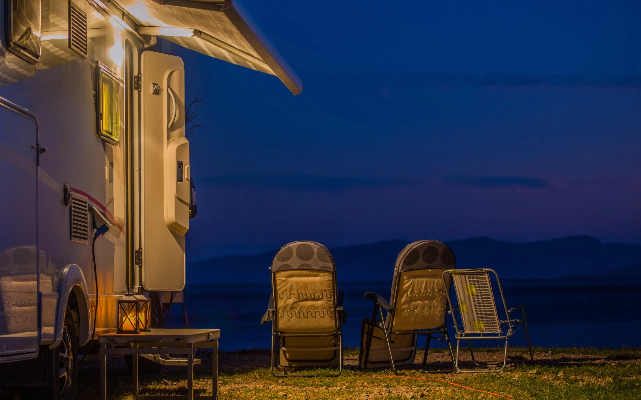 une roulotte illuminée et quelques chaises en montagne à la tombée de la nuit