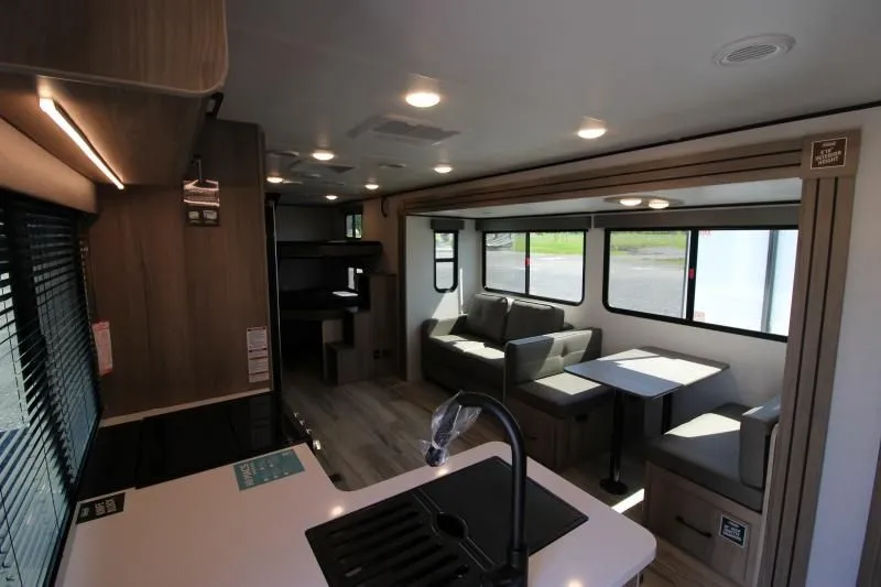 Intérieur lumineux de la roulotte Coleman 2900BH avec dinette, sofa convertible et cuisine moderne avec évier central.