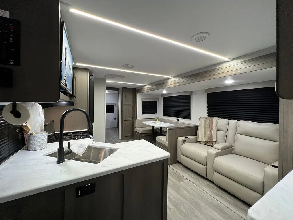 Vue intérieure de la roulotte Transcend 335BHT de Grand Design avec salon spacieux, divan double, banquette en U et cuisine équipée, éclairage LED au plafond.