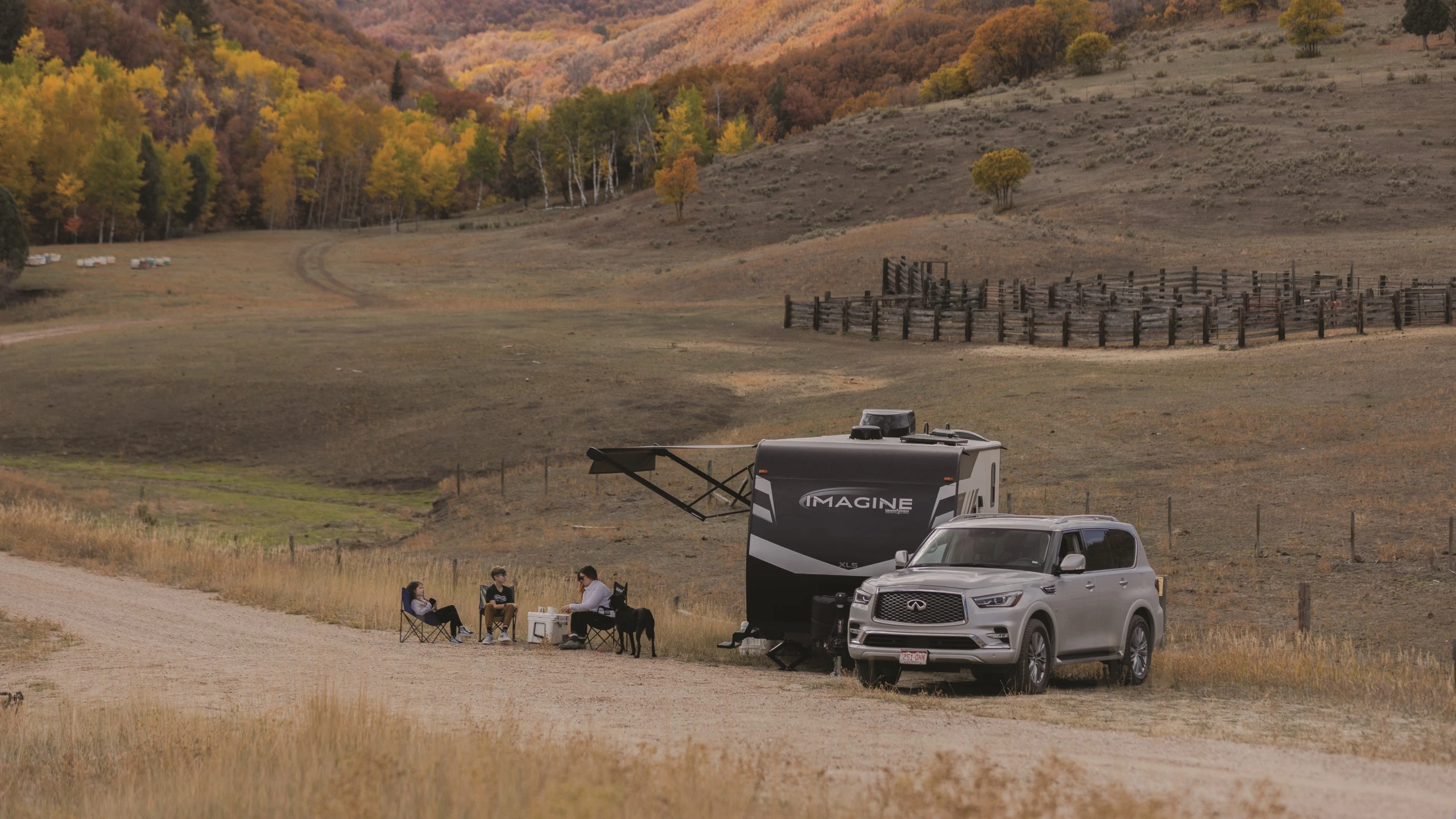 Roulotte Grand Design Imagine installée dans un champ automnal avec un VUS et un couple en plein air, illustrant la durabilité et la protection supérieure contre l’humidité.