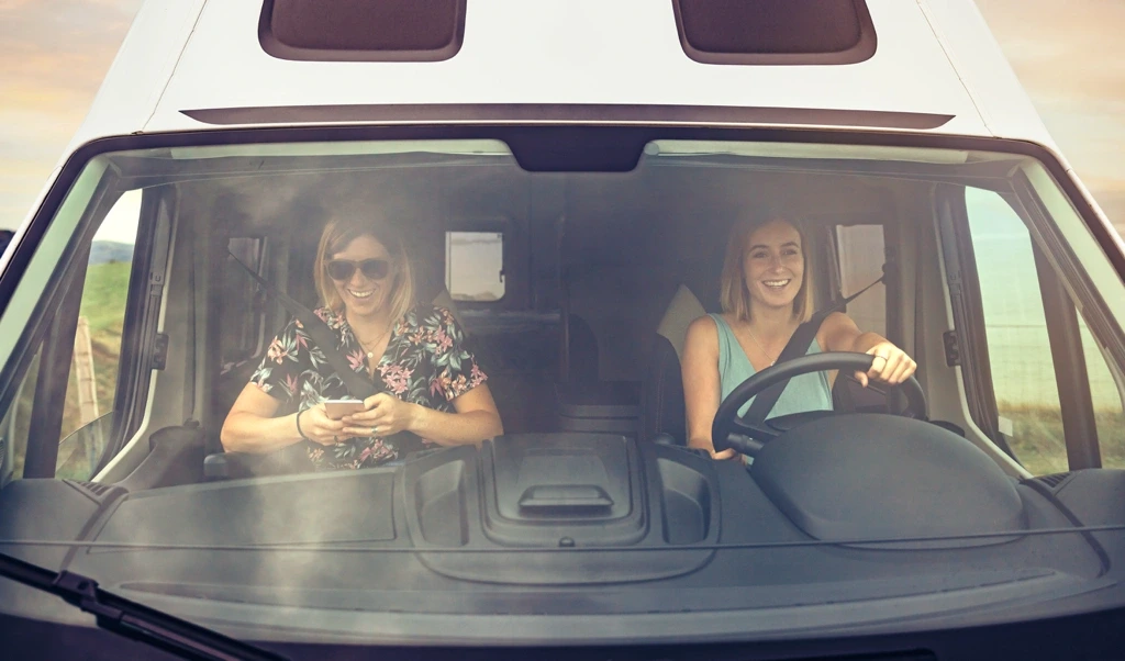 Deux femmes souriantes à bord d’un VR roulant sur une route canadienne, illustrant le plaisir et la liberté d’un road trip entre Montréal et Vancouver.