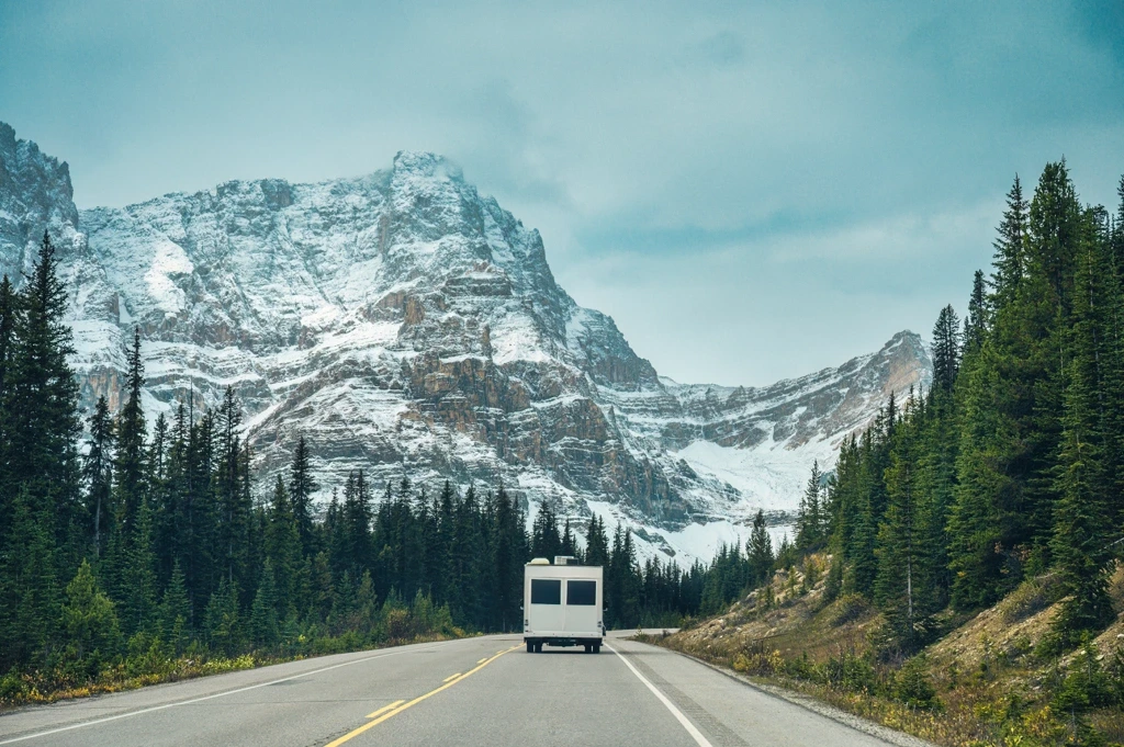 VR roulant sur une route des Rocheuses bordée de montagnes enneigées, illustrant la majesté du paysage albertain.