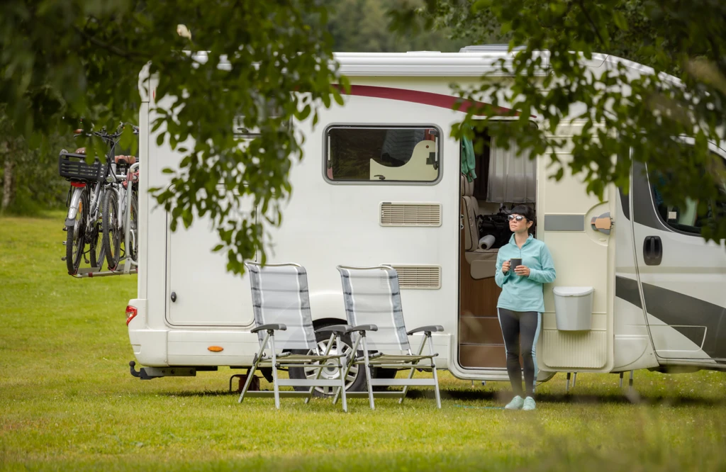 Roulotte installée sur un site de camping avec chaises et porte ouverte, illustrant le confort extérieur, l’autonomie et l’expérience de vie en roulotte.